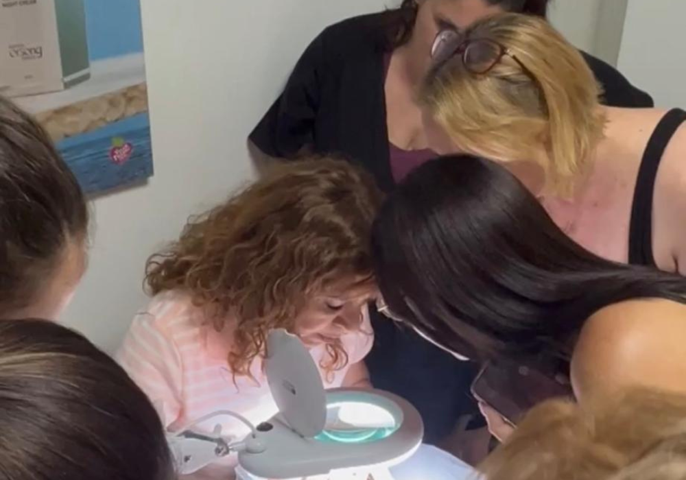 תלמידות בקורס צופות בהדגמה מעשית מול מנורת הגדלה מקצועית