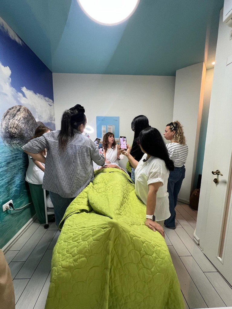 הדגמה קבוצתית סביב מיטת טיפול בקורס קוסמטיקה מקצועית